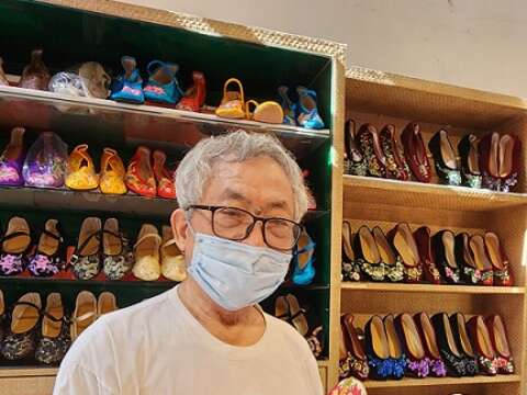 李东志手上拿着为台南市正觉寺法会设计的绣花鞋，鞋面上的莲花刺绣象徵「步步生莲」。（郑佩雯拍摄）