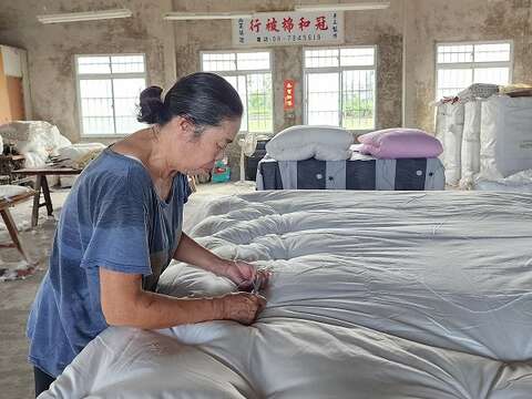 冠和的老师傅挥汗工作，将内胎被套与棉花缝合固定，从角落下针逐渐往内，双人被一共需61针，缝合点不管从哪个角度看都呈直线，全凭经验，无需丈量。（郑佩雯拍摄）